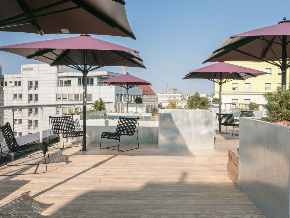Dachterrasse mit Holzdeck, Sitzmöbeln und großen Sonnenschirmen, Blick auf umliegende Stadtgebäude