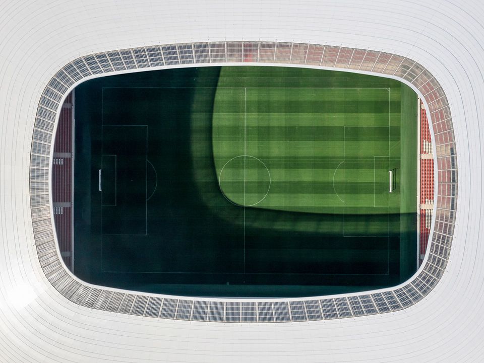 Draufsicht auf das Stadionoval mit durchgehender Dachkante, umlaufenden Tribünen und klar lesbaren Spielfeldmarkierungen, die die Geometrie und Kapazitätsringe zeigen.