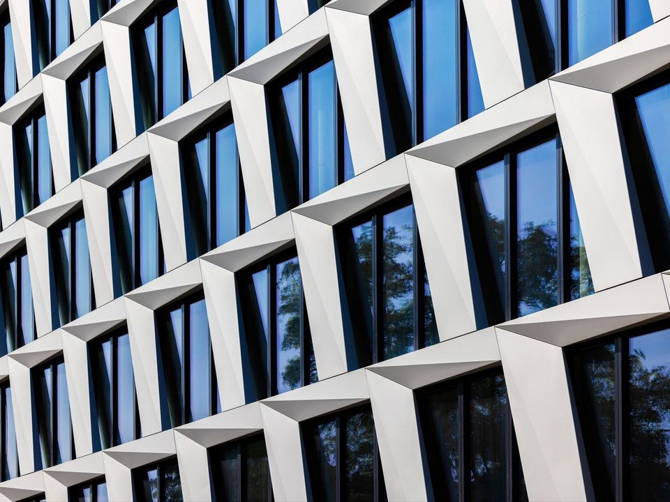 Detailansicht einer Fassade mit markanten, schräg gestellten Fensterrahmen und tiefen Laibungen, dynamische Geometrie und klare Linien