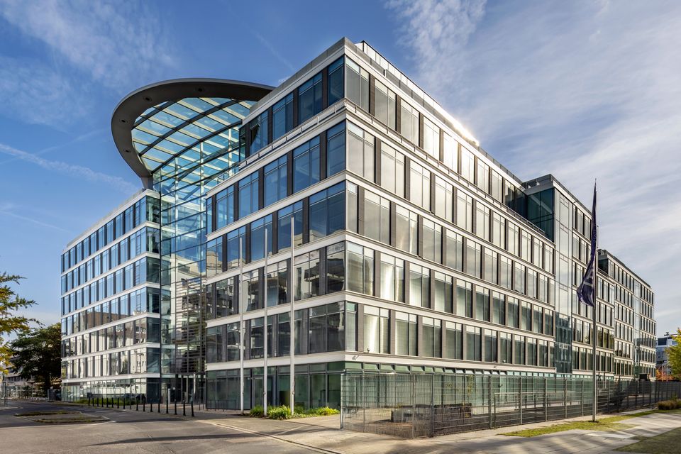 Außenaufnahme eines modernen Bürogebäudes mit klar gegliederter Glasfassade, zurückgestaffelten Geschossen und großem verglasten Atriumbereich an der Gebäudeecke.