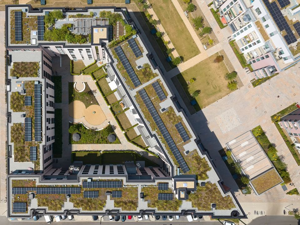 Draufsicht auf einen begrünten Wohnblock mit Innenhof, Dachgärten, Solaranlagen und umlaufender Wege- und Spielstruktur.