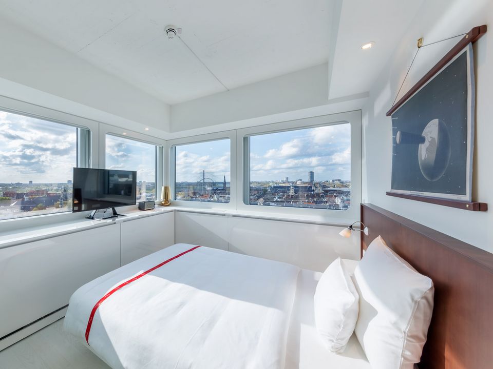 Hotelzimmer mit großem Fensterpanorama, weißem Bett und minimalistischem Interieur, Blick auf Stadtlandschaft