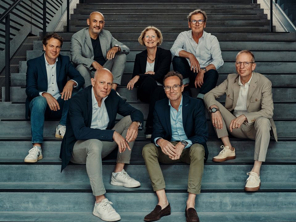 Gruppenaufnahme mehrerer Personen auf einer breiten Treppe in einem modernen Gebäude, umgeben von offenem Stahl- und Betontragwerk.