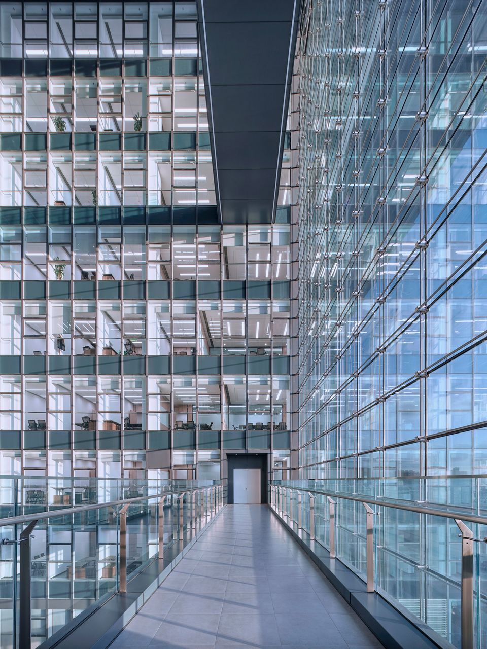 Innenaufnahme eines Erschließungsstegs innerhalb eines mehrgeschossigen Atriums mit umlaufenden Glasfassaden, modularer Bürostruktur und hoher räumlicher Transparenz.