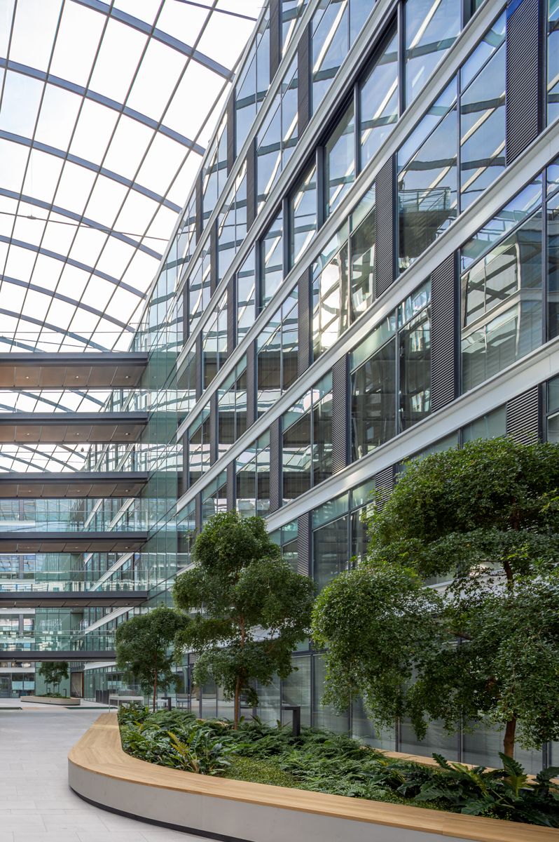 Atrium mit Glasdach und üppiger Begrünung, flankiert von modernen Büroflächen mit großen Fensterfronten