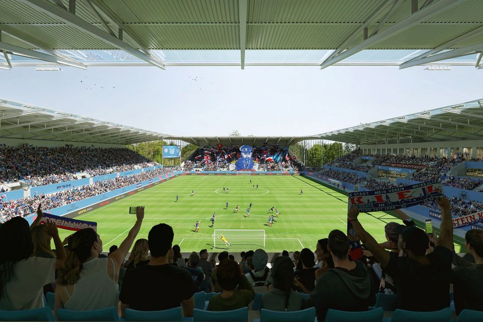 Innenaufnahme eines modernen Fußballstadions mit Blick von der Tribüne auf das Spielfeld, voll besetzte Ränge und dynamische Spielszene während einer Partie.