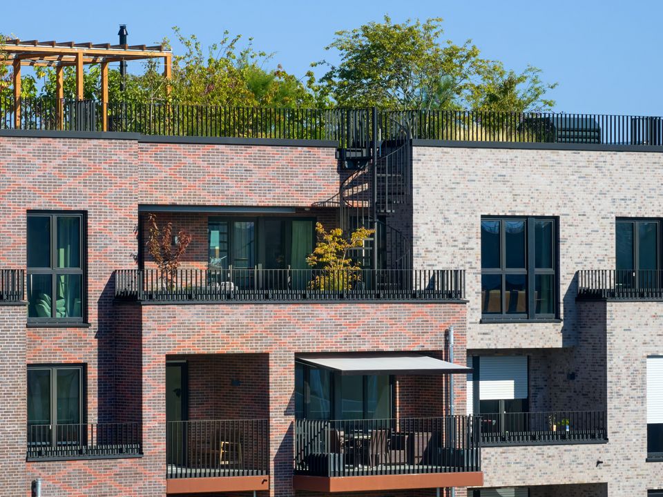 Detailaufnahme der Wohnfassade mit gestaffelten Balkonen, großformatigen Fenstern und begrünten Dachbereichen als Teil eines modernen Quartiers.