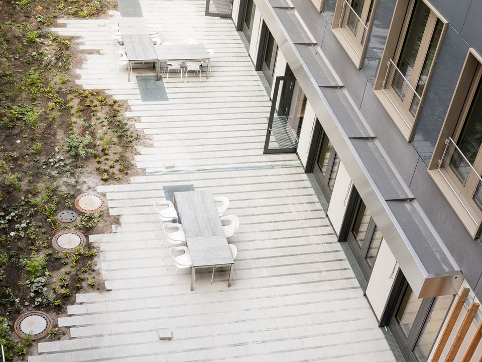 Courtyard with light-coloured stone slabs, seating areas and adjoining building façade, open design with green spaces