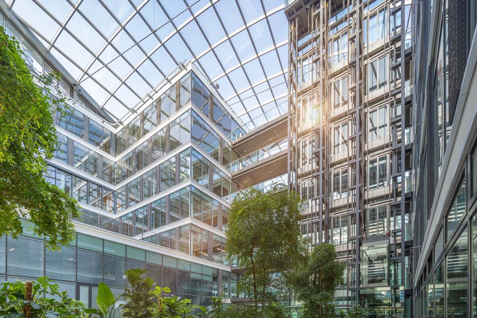 Großzügiges Atrium mit Glasdach und mehrgeschossigen Büroflächen, offene Architektur mit integrierter Begrünung