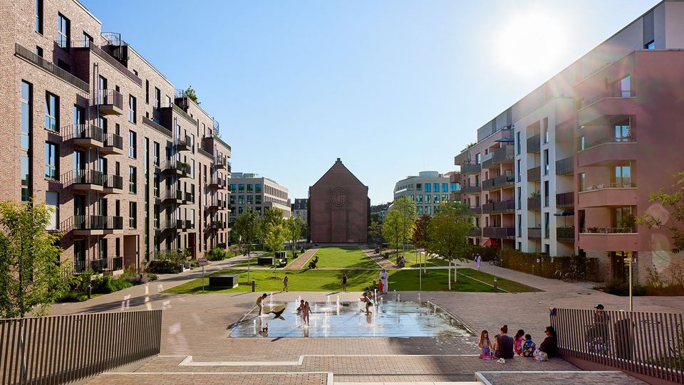 Blick auf ein urbanes Wohnquartier mit mehrgeschossigen Wohngebäuden und zentralem Grün- und Wasserbereich.