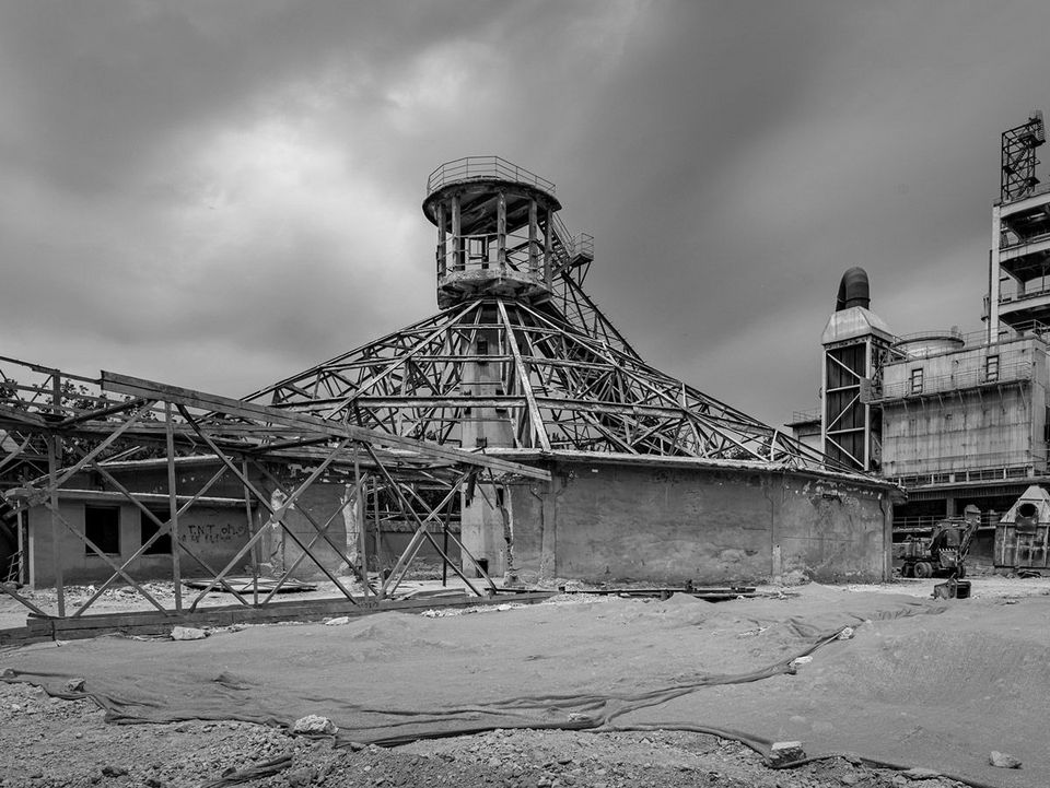 Historische Aufnahme einer weitläufigen Industrieanlage mit offenliegendem Stahltragwerk, zentralem Turmelement und massiven Bestandsbauten, die den ursprünglichen Zustand der technischen Produktionsarchitektur dokumentiert.