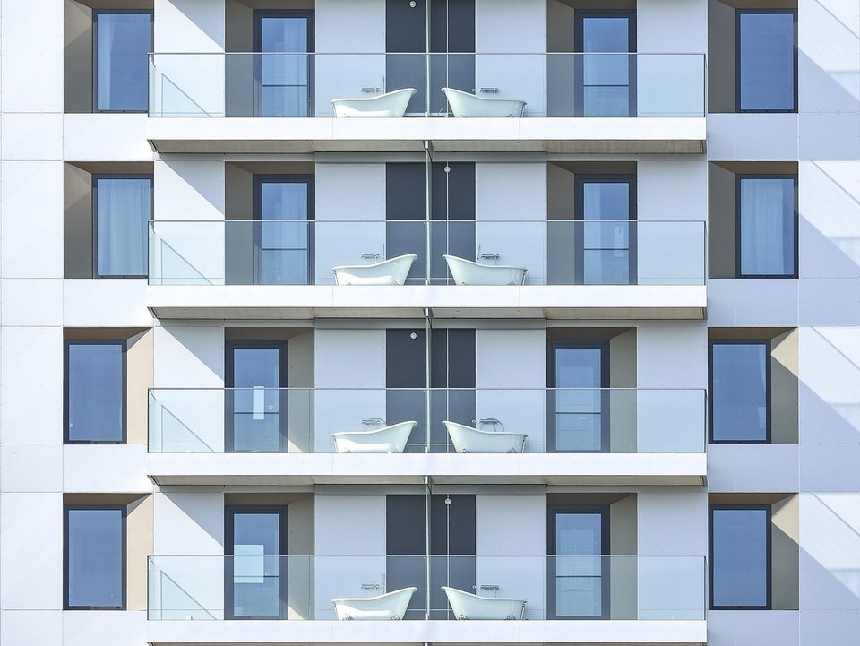 Frontansicht eines Wohngebäudes mit Balkonen und freistehenden Badewannen, klare Fassadengliederung mit Glasbrüstungen