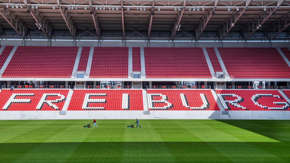 Innenansicht des Stadions mit roten Sitzreihen und Schriftzug FREIBURG, gepflegtes Spielfeld unter weit gespanntem Dach