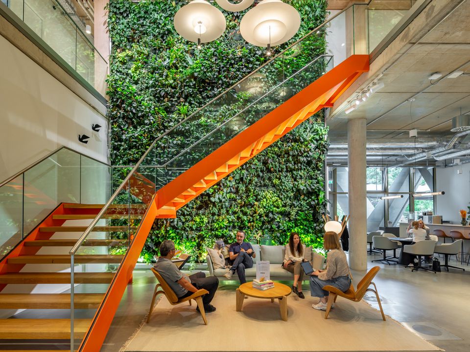 Lounge area in front of a vertical plant wall with striking stairs in bold orange, open room design with seating areas