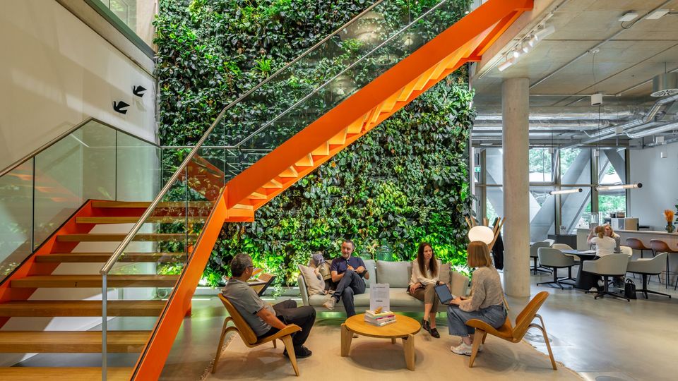 Lounge-Bereich vor vertikaler Pflanzenwand mit markanter Treppe in kräftigem Orange, offene Raumgestaltung mit Sitzgruppen