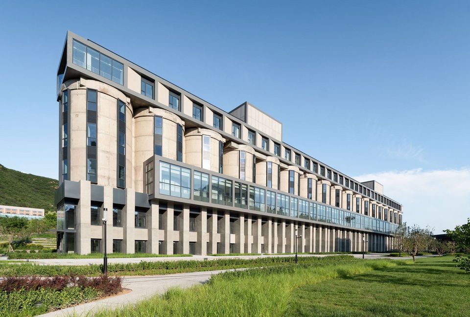 Langgestrecktes Gebäude mit integrierten Silos und moderner Glasfassade, industrielle Architektur in grüner Landschaft