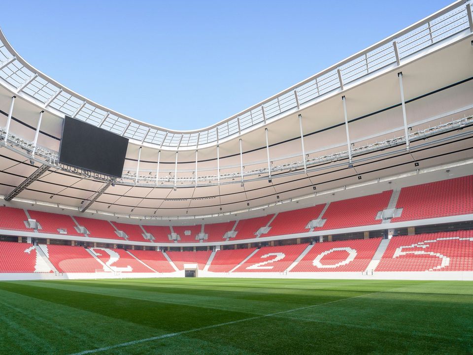Innenaufnahme vom Spielfeld mit umlaufenden Tribünen, großformatigen Blockzahlen, frei gespannter Dachkante und gleichmäßiger Tageslichtsituation für TV‑Übertragungen.