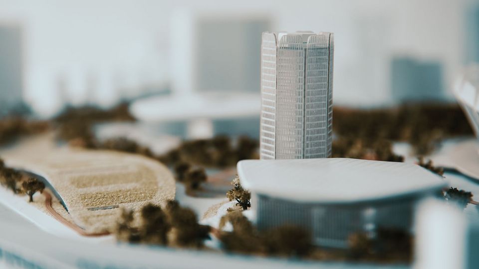 Detail view of an architectural city model featuring a tall tower volume, surrounding building structures, modelled landscape areas and pathway layouts.