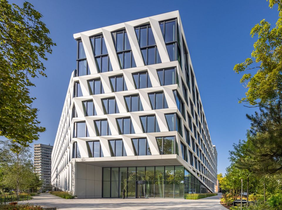 Frontansicht eines Bürogebäudes mit geometrisch strukturierter Fassade aus schrägen Fensterrahmen, klare Architektur vor blauem Himmel