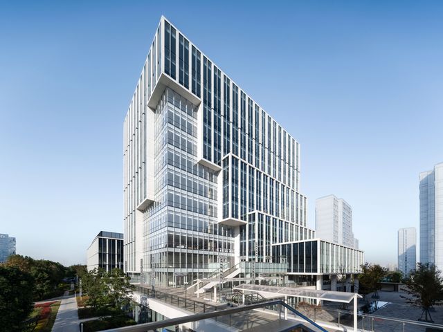 Außenaufnahme eines modernen Hochhausensembles mit markanter Glasfassade, gestaffelten Baukörpern und erhöhtem Eingangsbereich im urbanen Kontext.