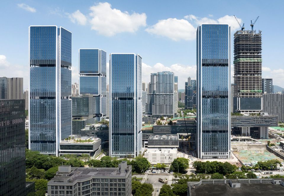 Luftaufnahme eines Ensembles aus mehreren Hochhaustürmen mit durchgehend verglasten Fassaden und begrünten Dachterrassen.