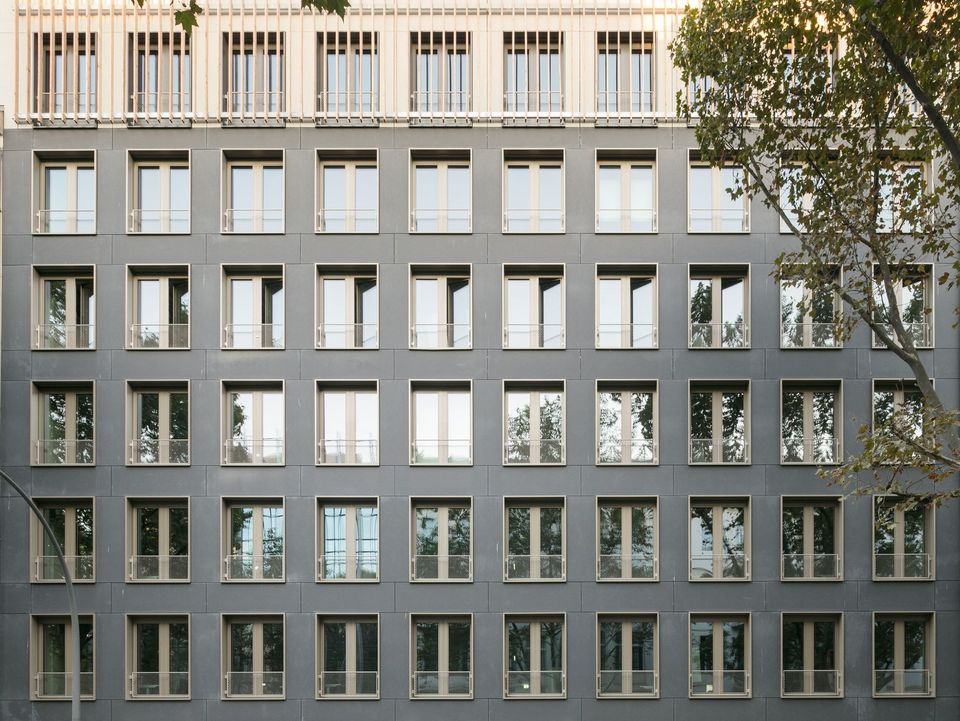 Fassadenansicht eines mehrgeschossigen Gebäudes mit regelmäßiger Fensteranordnung und dunkler Verkleidung, klare Rasterstruktur