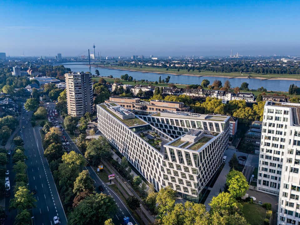 Luftaufnahme eines modernen Büroquartiers mit begrünter Dachlandschaft, klarer Gebäudestruktur und Blick auf das angrenzende Stadtgebiet sowie das Flussufer.