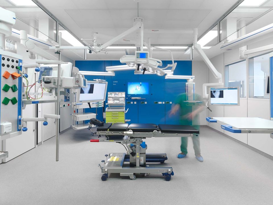 Operationssaal mit hochmoderner Ausstattung, Deckenarmen und Monitoren, sterile Umgebung in Weiß und Blau