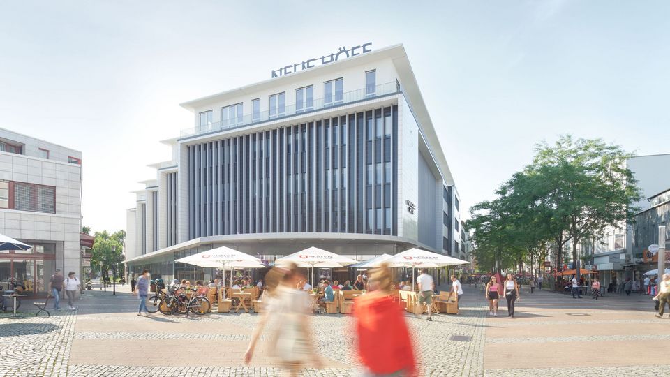 Außenansicht eines modernen Geschäftshauses mit vertikalen Fassadenelementen und großem Glasbereich, belebter Platz mit Außengastronomie und Sonnenschirmen