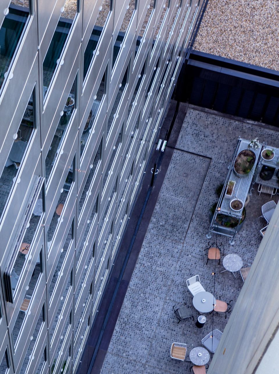 Blick in einen Innenhof zwischen Hochhausfassaden mit reflektierenden Glasflächen, unten Sitzgruppen und Pflanzkübel auf gepflastertem Boden