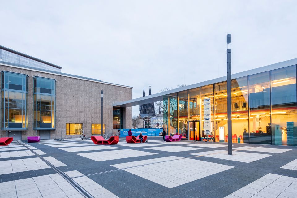 Moderner Vorplatz mit großer Glasfassade und farbigen Sitzmöbeln bei Tageslicht