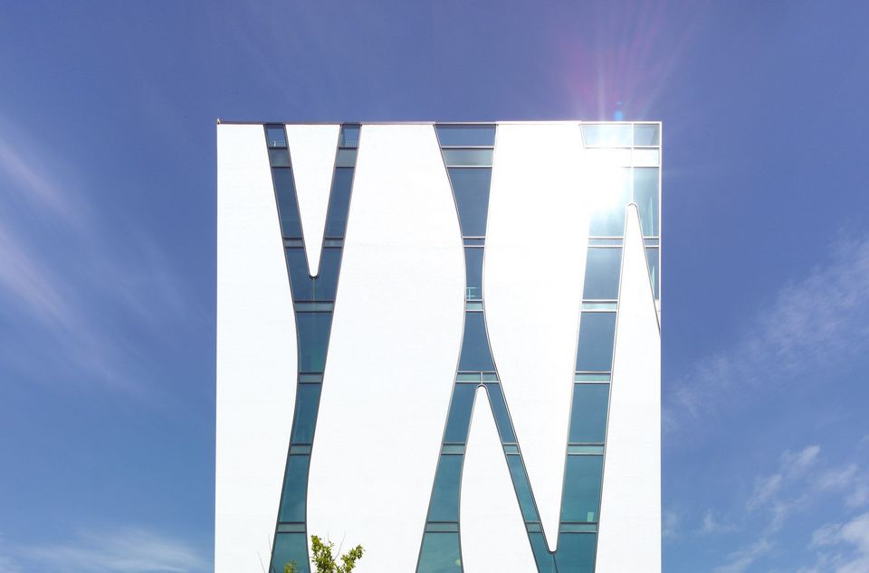 Detailansicht einer modernen Glasfassade mit organisch geschwungenen Streifen vor blauem Himmel