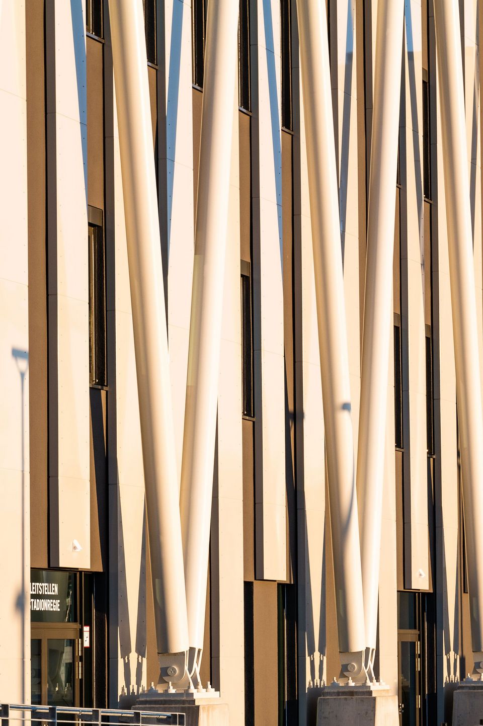 Detailansicht der Stadionfassade mit schräg angeordneten weißen Stahlstützen vor dunkler Wand, markante vertikale Struktur