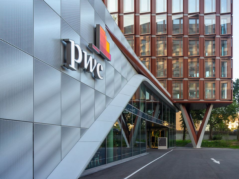Eingangsbereich eines Bürogebäudes mit schräger Metallfassade und PWC-Logo, markante Architektur mit roten Fassadenprofilen