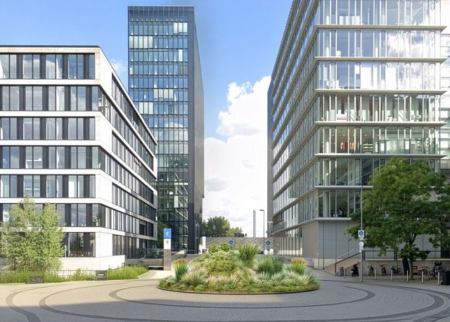 Außenaufnahme eines modernen Büroensembles mit zwei gläsernen Gebäuden, die einen begrünten Kreisverkehr fassen, mit klarer Wegführung und stadträumlicher Achse.