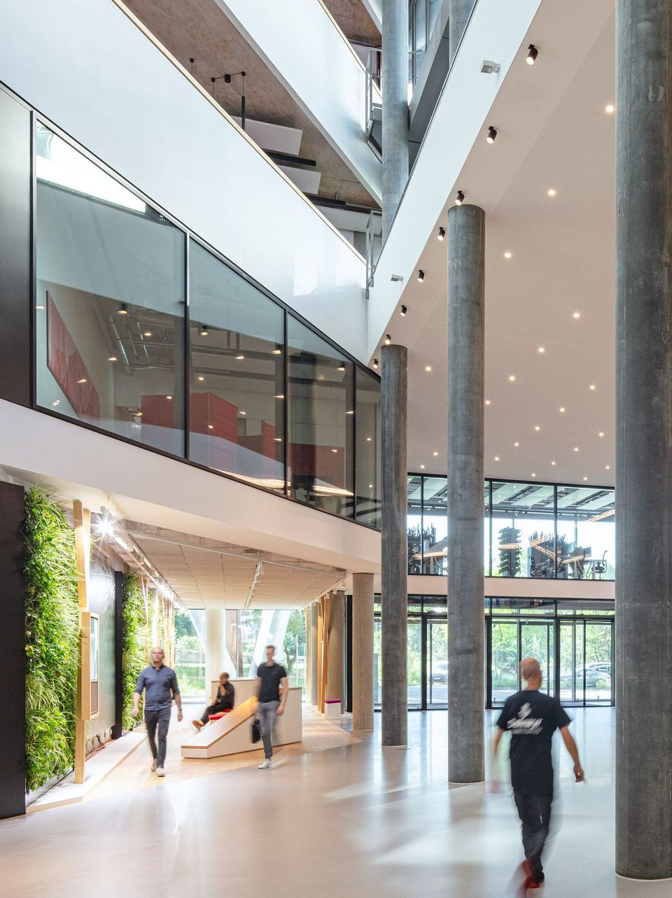 Großzügige Lobby mit hohen Glasfronten, Sichtbetonstützen und vertikaler Begrünung, offene Raumstruktur mit Galerieebenen