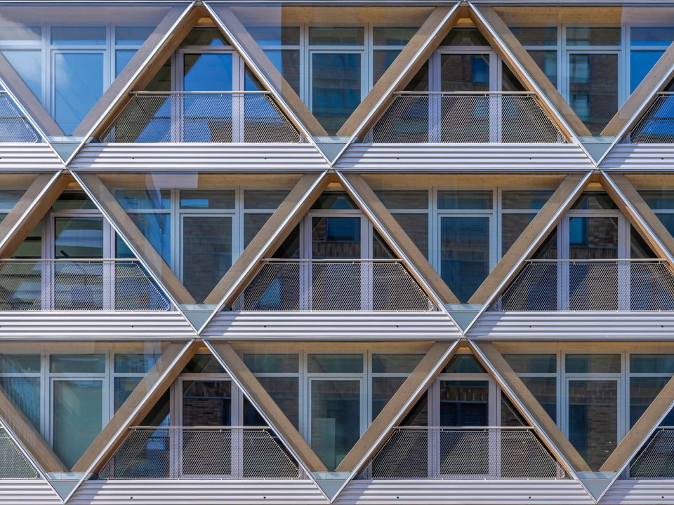 Fassadendetail mit geometrischen Dreiecksmodulen aus Holz und Metall, klare Linien und integrierte Balkonflächen