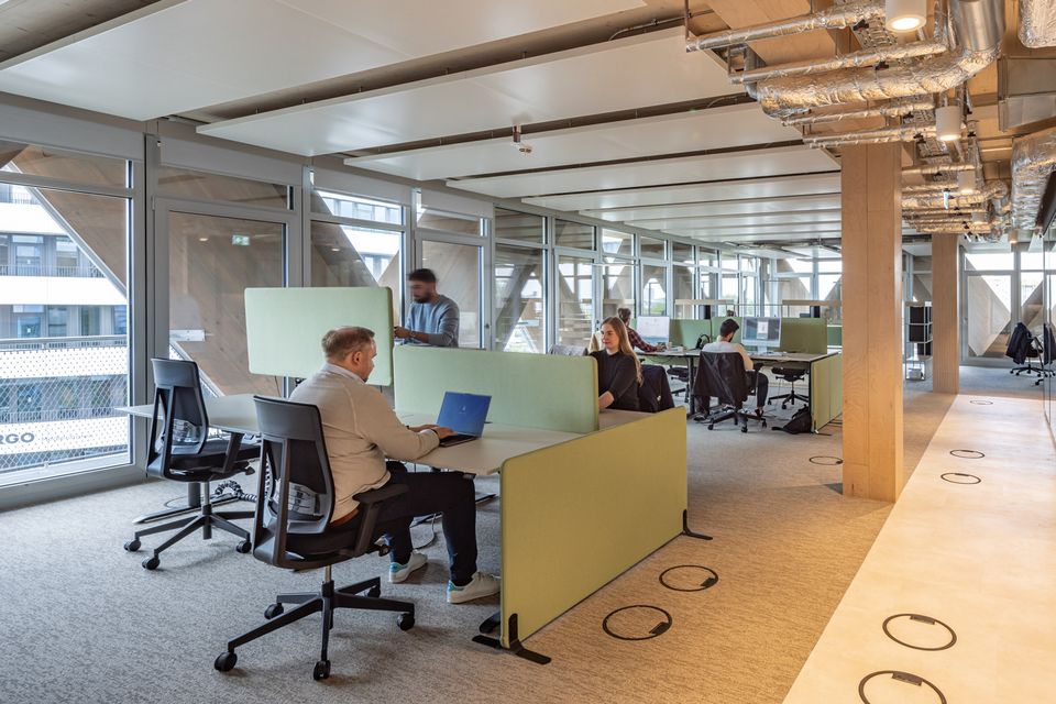 Open-plan office space with modular workstations, exposed technical ceiling and large glass fronts with triangular structure