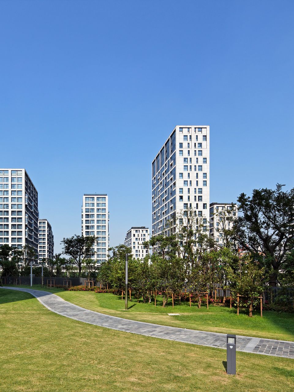 Grüne Parkfläche mit Gehweg vor modernen Wohnhochhäusern im Expo Village Shanghai.