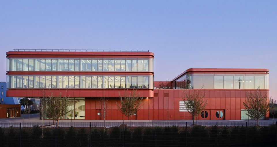 Frontalansicht des Forschungs- und Entwicklungszentrums mit großformatiger Glasfassade, klarer Kubatur und glatter Metallverkleidung im städtischen Umfeld.