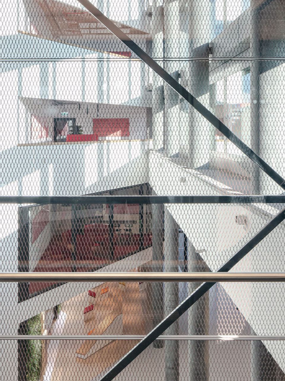 Innenansicht eines Atriums mit diagonalen Metallstreben und offenen Galerieebenen, Blick auf rote Akzente im Raum
