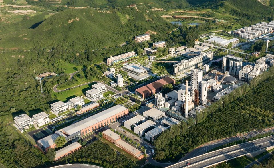 Luftaufnahme eines großflächigen Wissenschafts- und Gewerbecampus mit Laborgebäuden, Produktionsbereichen, begrünten Achsen und umlaufender Infrastruktur.