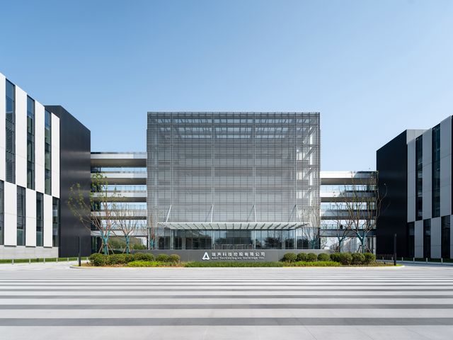 Außenaufnahme eines modernen Forschungs- und Bürogebäudes mit klar gegliederter Fassadenstruktur, lamellenartigem Sonnenschutz und großzügigem Vorplatz mit Begrünung.
