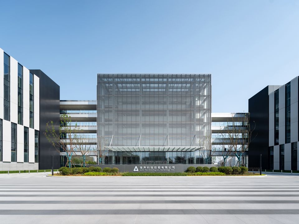 Außenaufnahme eines modernen Forschungs- und Bürogebäudes mit klar gegliederter Fassadenstruktur, lamellenartigem Sonnenschutz und großzügigem Vorplatz mit Begrünung.