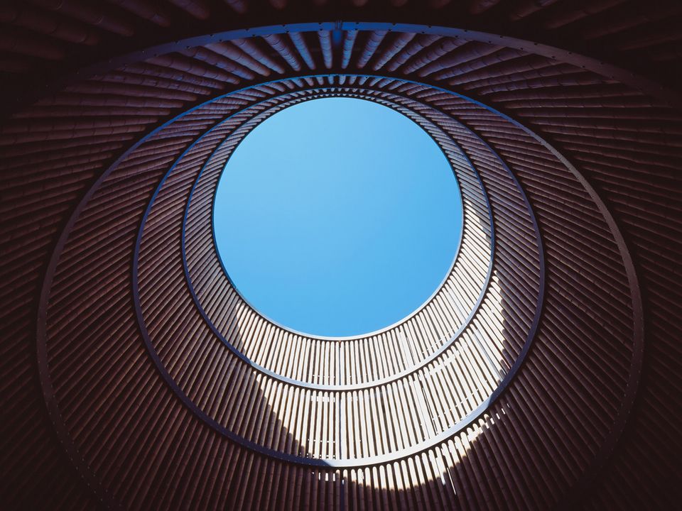 Blick nach oben durch kreisförmige Öffnung in Holzlamellenstruktur des Parkhauses, dynamische Lichtwirkung und klare Geometrie