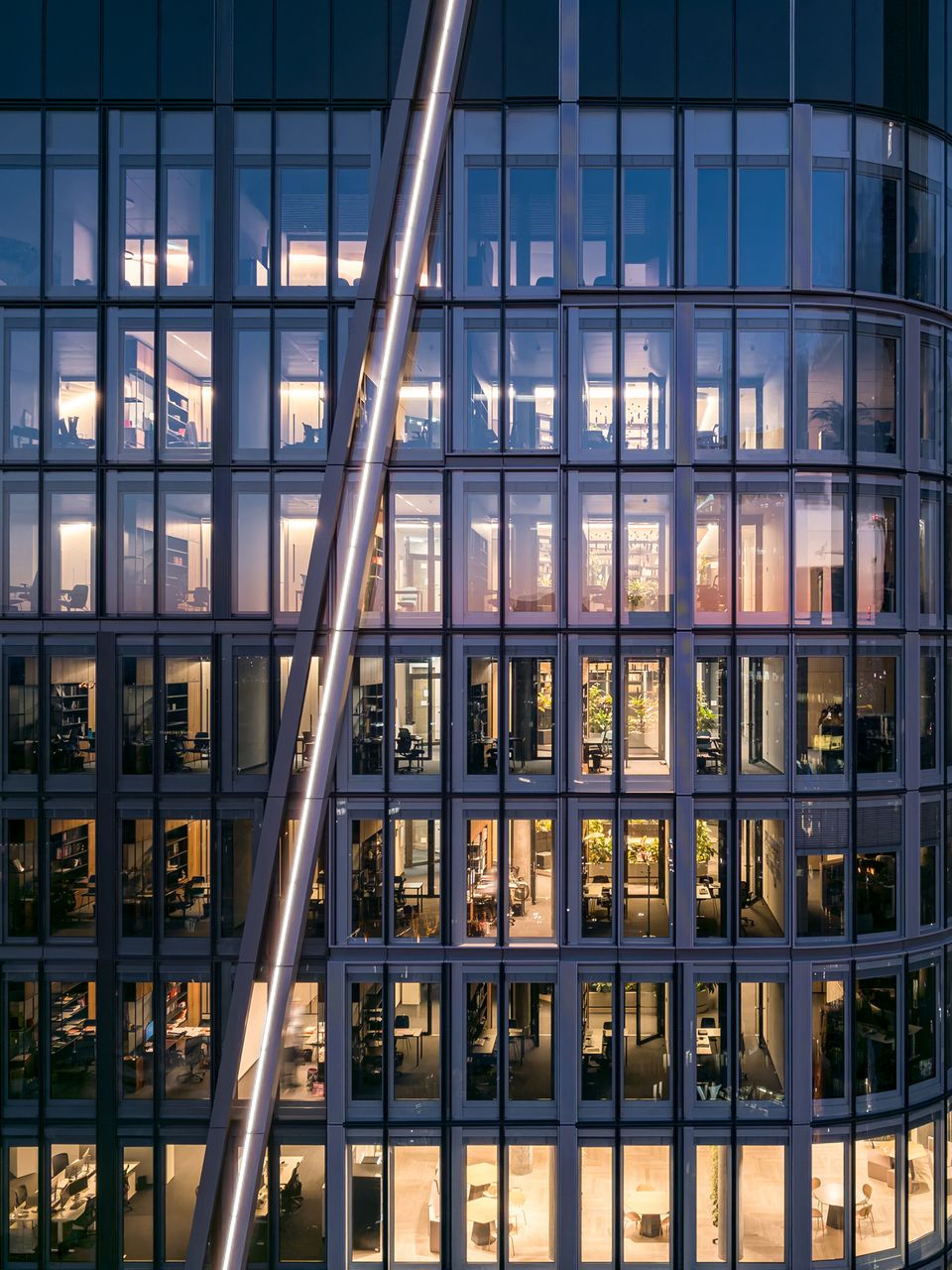 Detailaufnahme einer Hochhausfassade mit modularen Fensterreihen, tiefen Gebäudeneinschnitten und Einblicken in mehrgeschossige Büro- und Aufenthaltsbereiche.