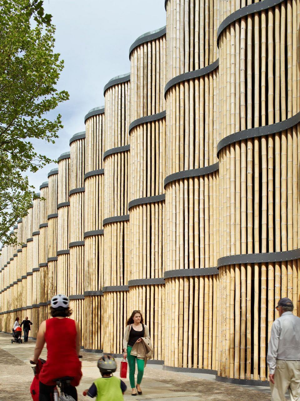 Lange wellenförmig geschwungene Parkhausfassade aus vertikalen Holzlamellen, rhythmische Architektur entlang eines Gehwegs