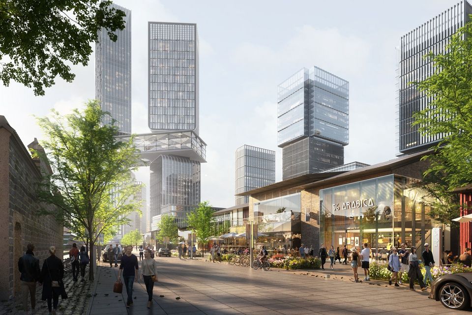 Straßenperspektive eines urbanen Quartiers mit gemischt genutzten Gebäuden, belebten Freiflächen, Gastronomiebereichen und einem markanten Hochhausensemble im Hintergrund.