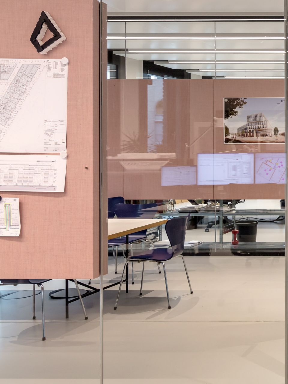 Innenaufnahme eines Planungsraums mit gläserner Trennwand, an der technische Zeichnungen und Visualisierungen befestigt sind.