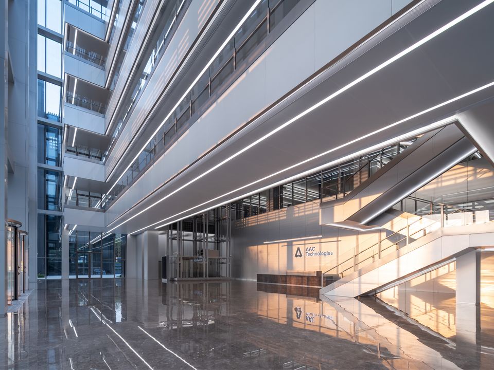 Innenaufnahme eines mehrgeschossigen Atriums mit offenen Galerieebenen, linearen Lichtbändern und gläsernen Fassadenflächen in einem modernen Unternehmensgebäude.